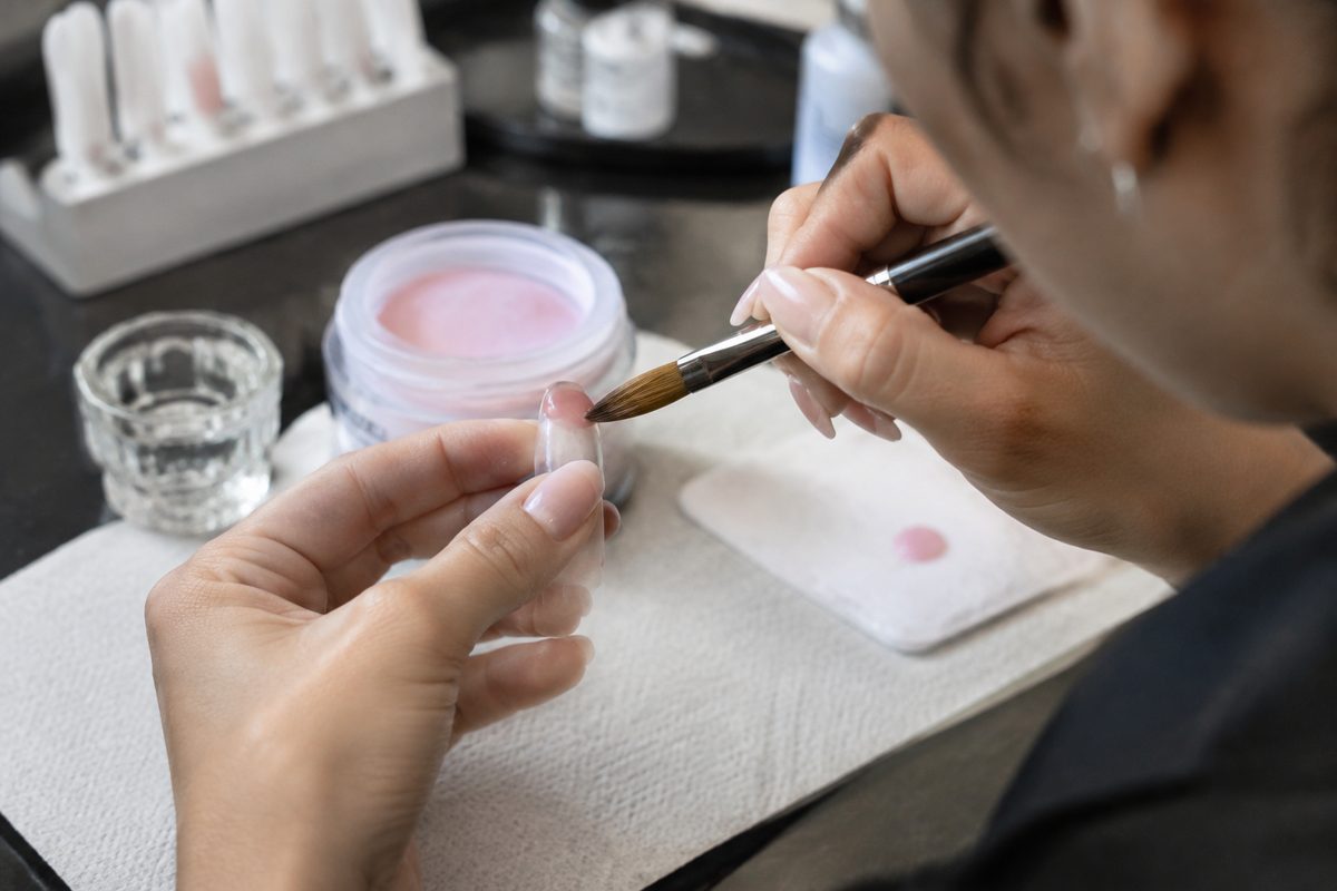 Master technician sculpting an acrylic nail extension with a fine brush and monomer bead